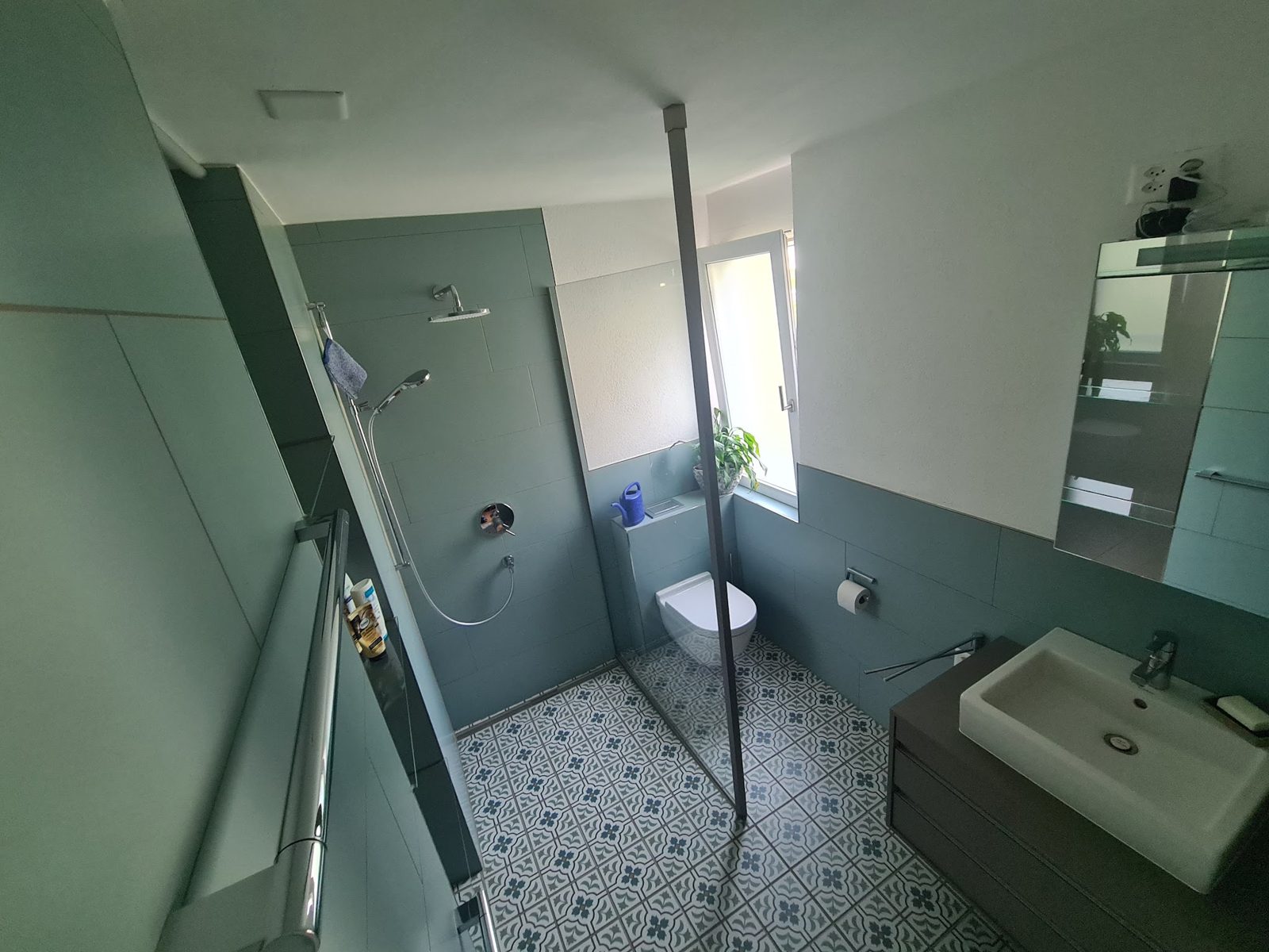 Frisch umgebautes Badezimmer mit grünen Wandplatten und gemusterten Bodenfliesen