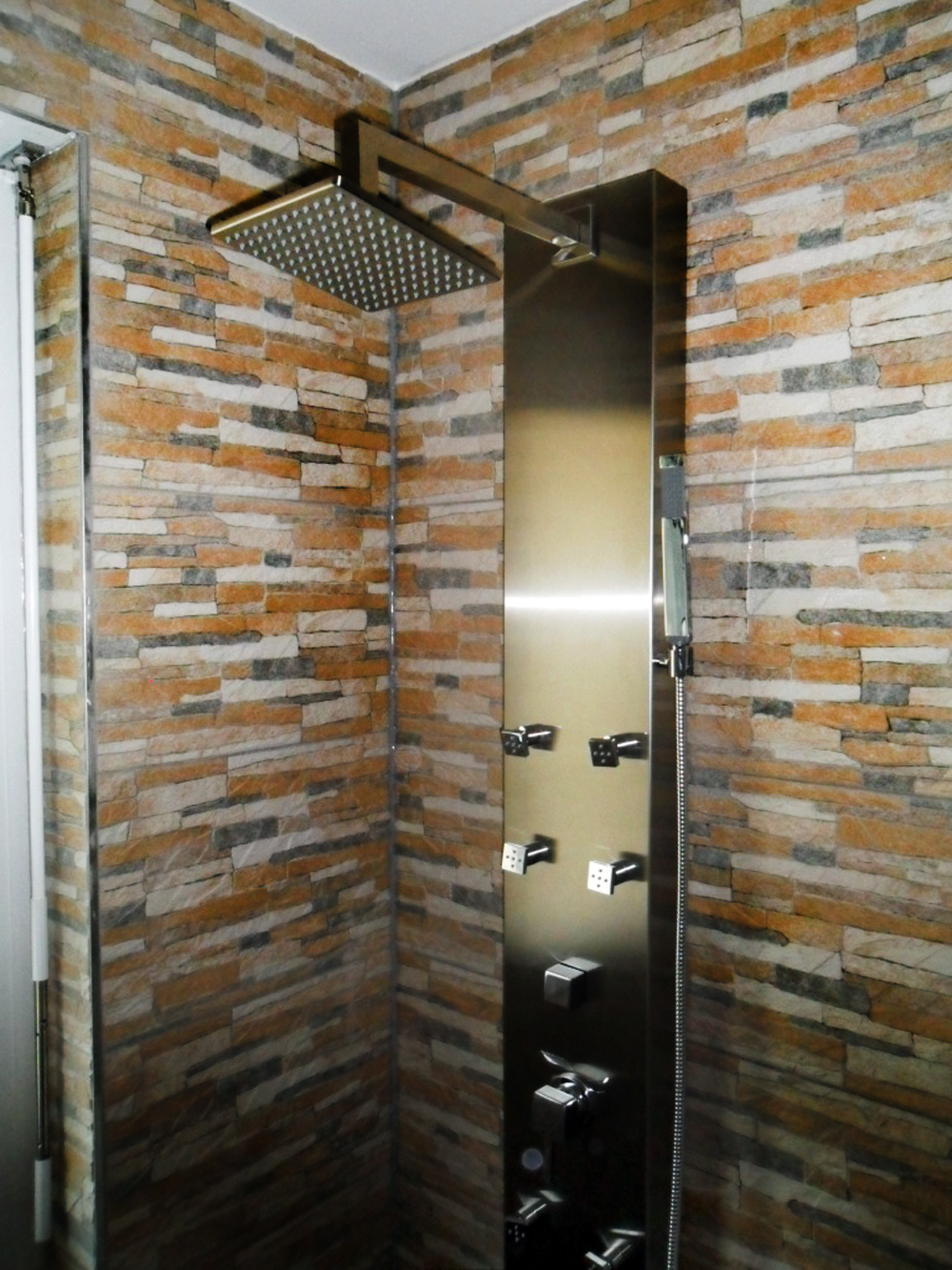 Dusche mit farbiger Natursteinwand und Regendusche