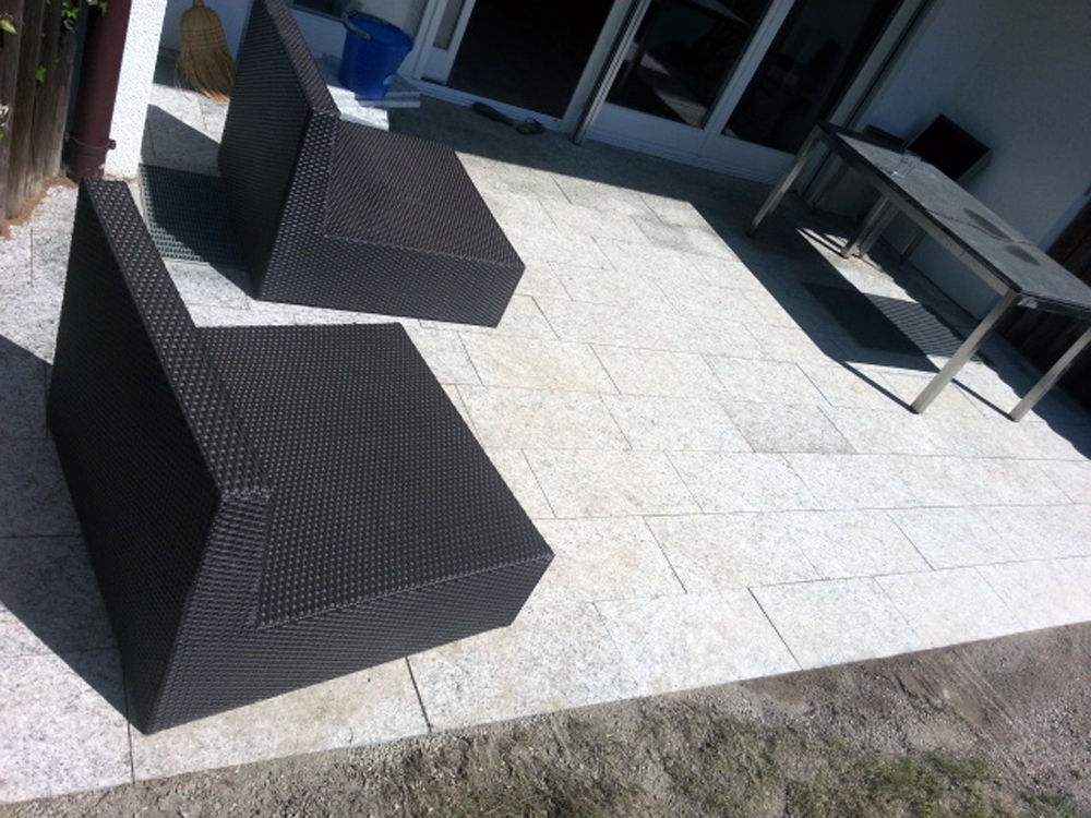 Terrasse mit hellen Natursteinplatten und Loungemöbeln